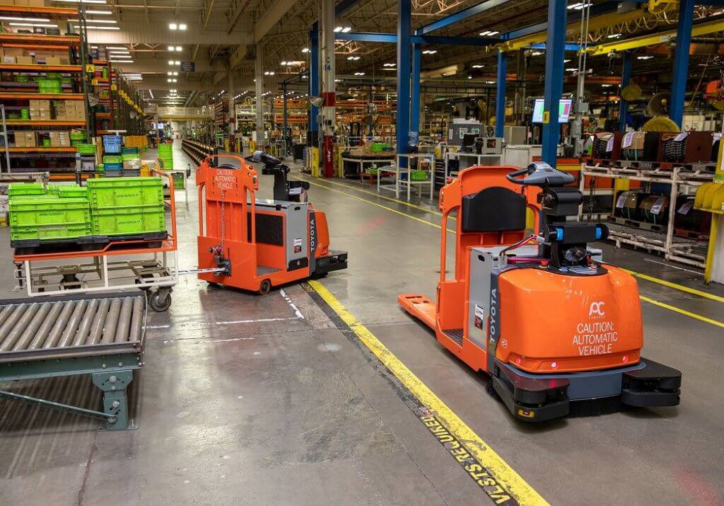 Orange automated guided vehicles moving materials along a factory aisle